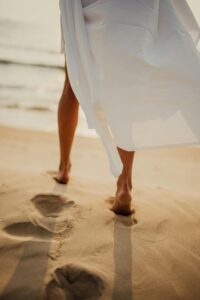 Woman walking barefoot along beach by ocean